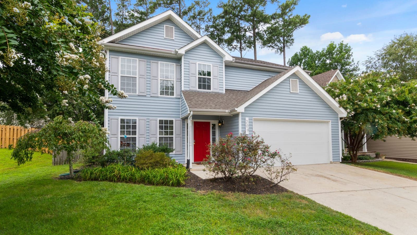 A light blue two story home with a red front door, a green lawn, and flowering trees in the yard